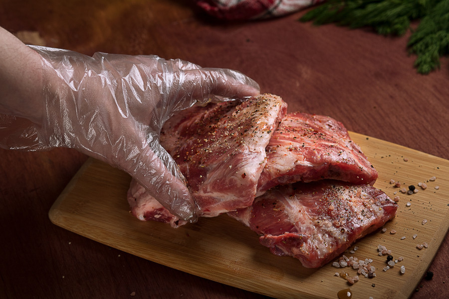 Ręka osoby w jednorazowej rękawiczce zrywce trzymająca kawałek przyprawionego mięsa - niupak.eu